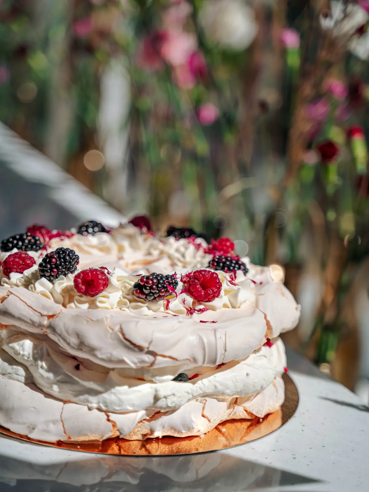 Tort bezowy przyozdobiony bitą śmietaną i owocami leśnymi.